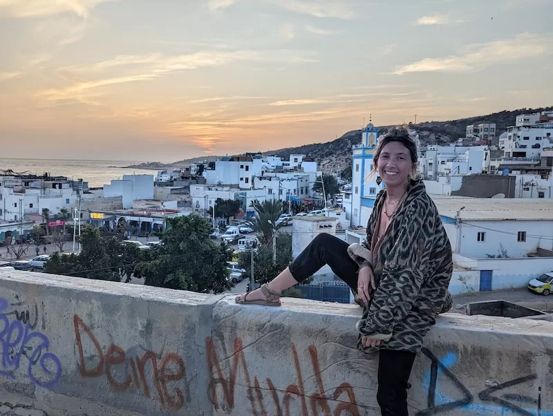 Woman sitting on a wall overlooking a coastal Moroccan town at sunset