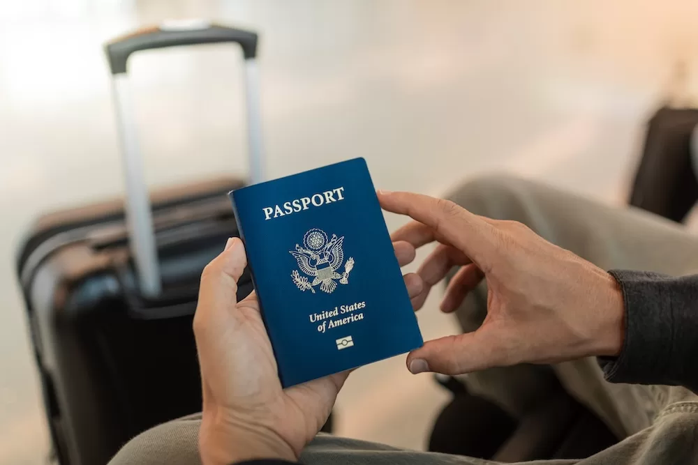 Traveler holding a U.S. passport beside packed luggage