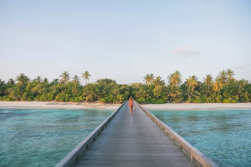 Woman walking along a jetty toward a tropical island