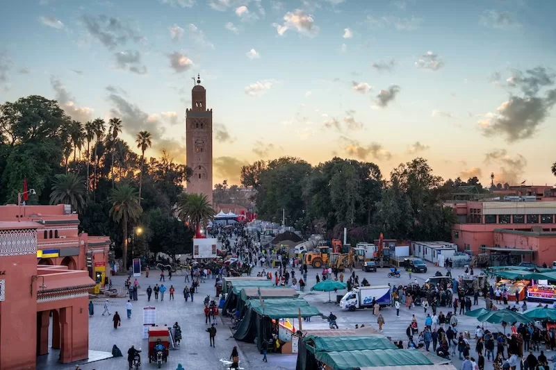 Busy Marrakech square at sunset with mosque tower and market stalls