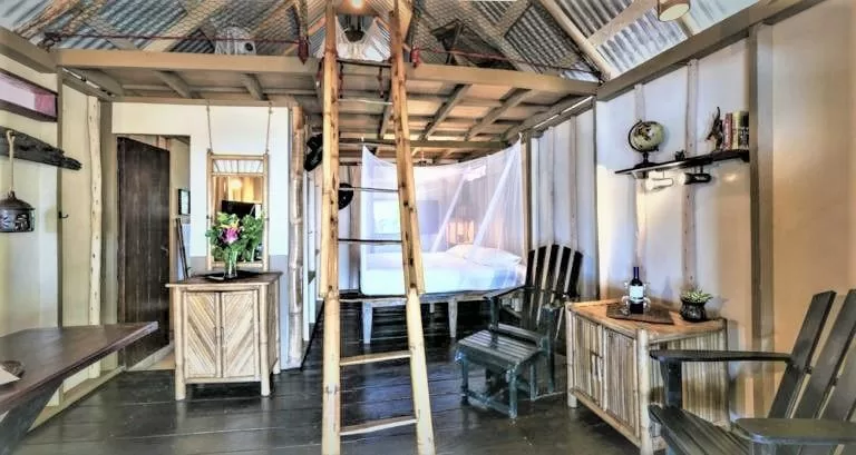 Rustic bungalow interior with a mosquito-net bed, bamboo furniture and loft ladder.