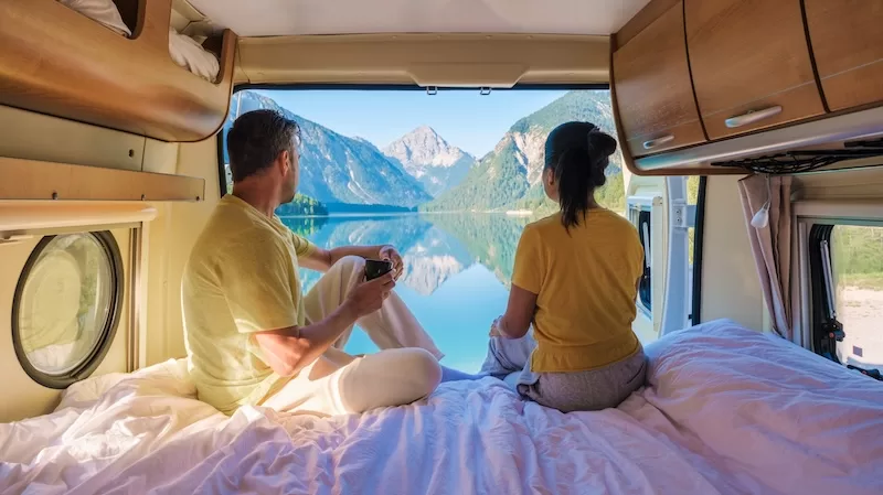 Couple working and travelling from a campervan beside an alpine lake