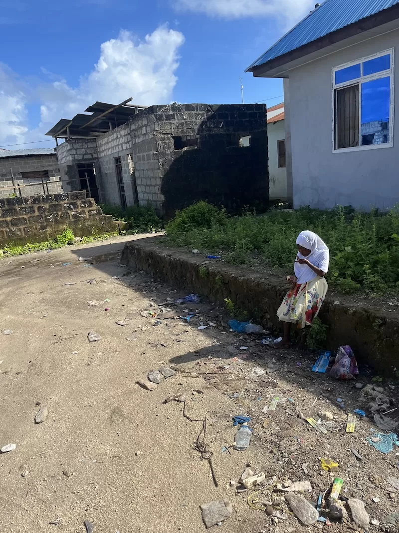 A local street in Zanzibar showing a child seated near buildings and roadside litter.