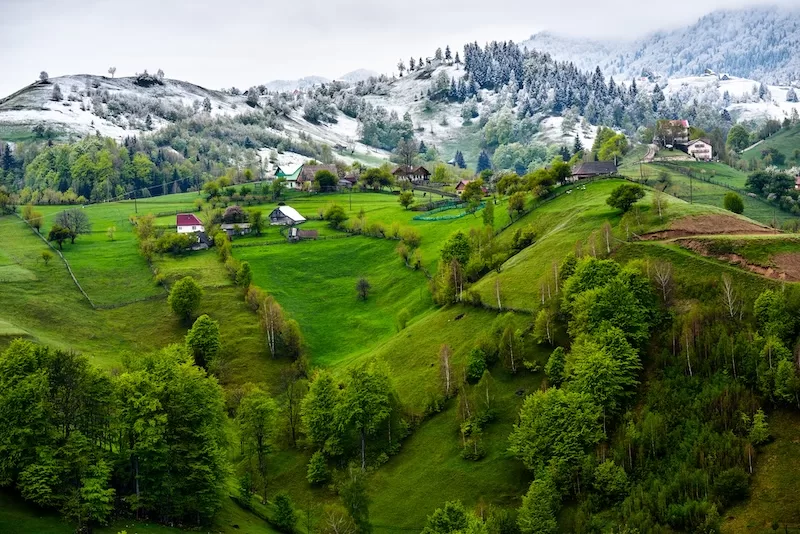 Snow-dusted green hills and rural homes in the Transylvania Highlands