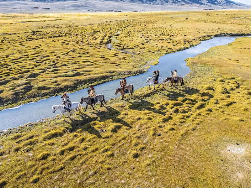 Horse riders crossing remote grasslands beside a mountain river