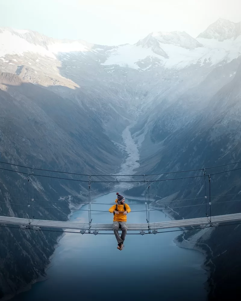 Traveller sitting on a suspension bridge above a mountain lake