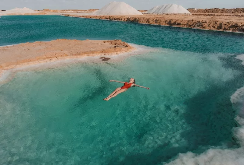 Turquoise salt lake with desert landscape and a person floating in clear water