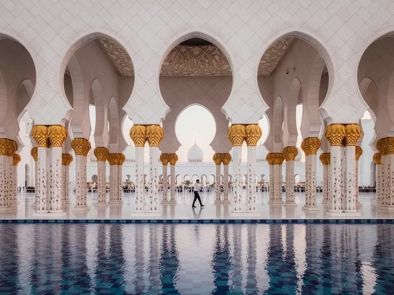 Ornate mosque interior with white arches and reflective marble floor
