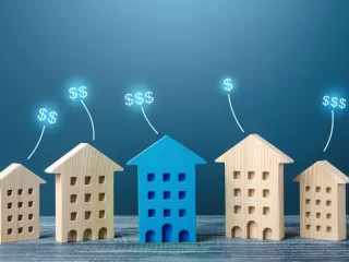 Wooden house models of increasing size with rising dollar signs, representing growing asset value