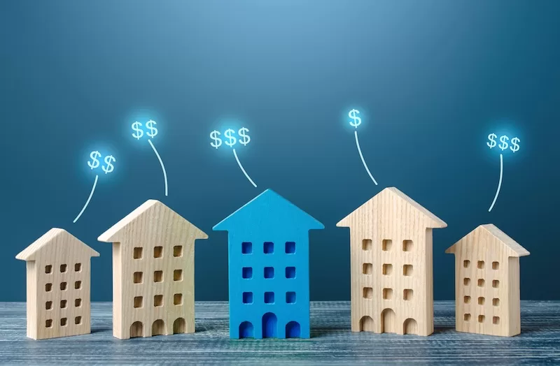 Wooden house models of increasing size with rising dollar signs, representing growing asset value