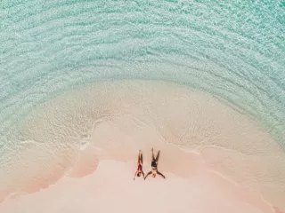 Aerial view of a couple lying on a pink sand beach in shallow turquoise water