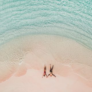 Aerial view of a couple lying on a pink sand beach in shallow turquoise water
