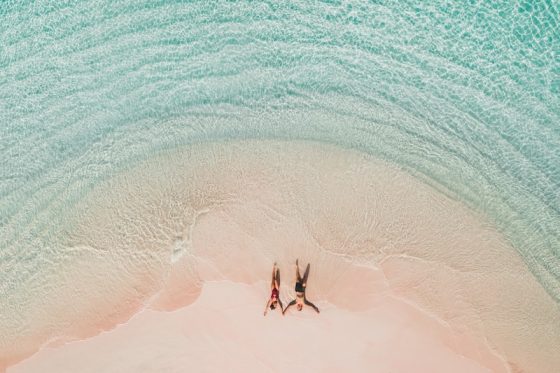 Aerial view of a couple lying on a pink sand beach in shallow turquoise water