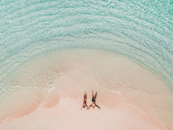 Aerial view of a couple lying on a pink sand beach in shallow turquoise water