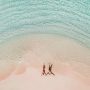 Aerial view of a couple lying on a pink sand beach in shallow turquoise water