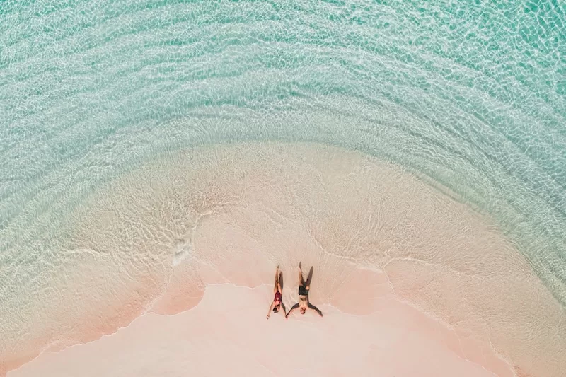 Aerial view of a couple lying on a pink sand beach in shallow turquoise water