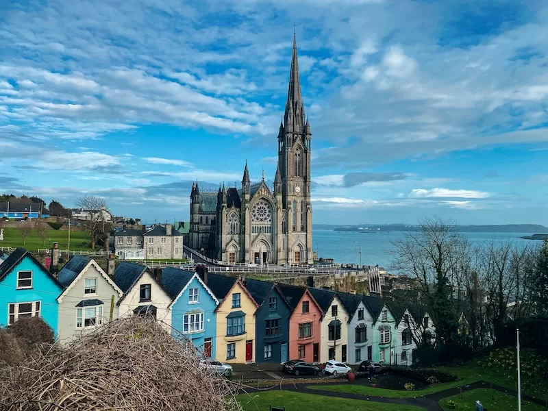 Colorful row houses beneath a Gothic cathedral overlooking the harbor in Cobh, Ireland