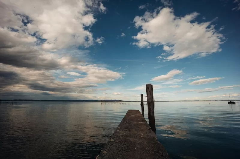 Pier extending into calm water under a wide cloudy sky