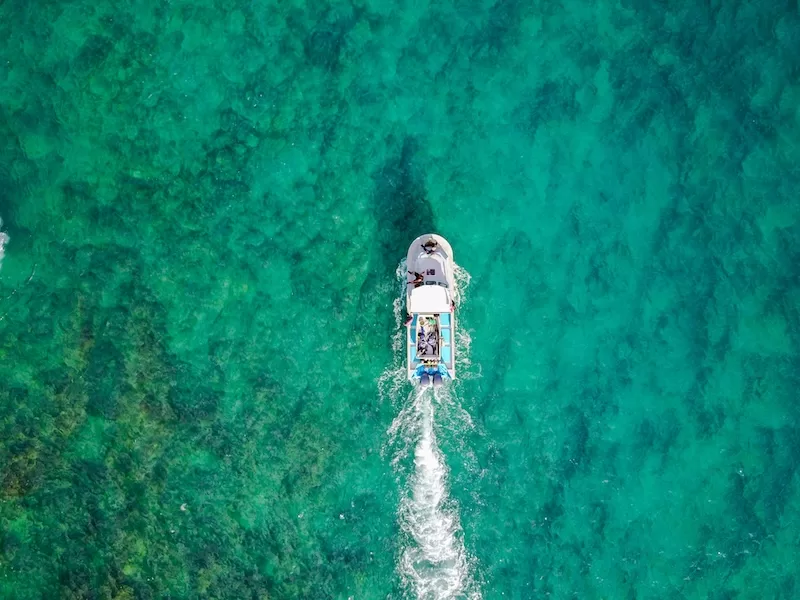 Aerial view of a boat leaving a wake through clear turquoise water over a coral reef