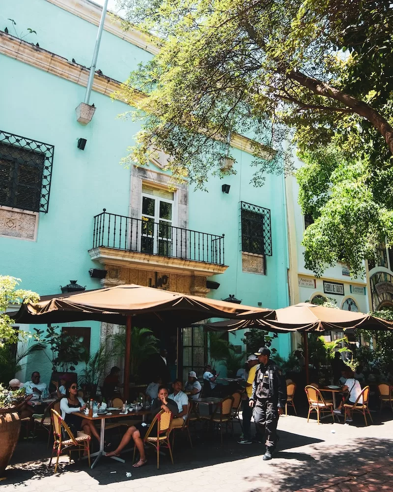 Outdoor café beneath a tree in front of a teal colonial building in Santo Domingo's Zona Colonial