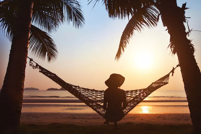 Silhouette of a person relaxing in a hammock between palm trees at sunset