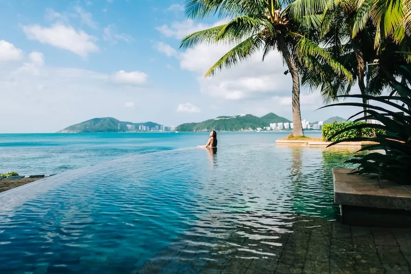 Woman relaxing in an infinity pool overlooking a tropical bay and mountains