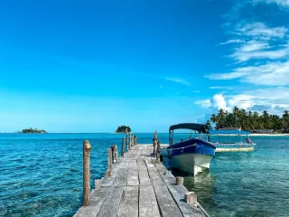 Wooden dock leading to a moored boat in the clear turquoise waters of the San Blas Islands, Panama
