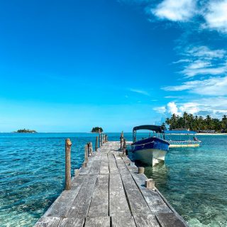 Wooden dock leading to a moored boat in the clear turquoise waters of the San Blas Islands, Panama