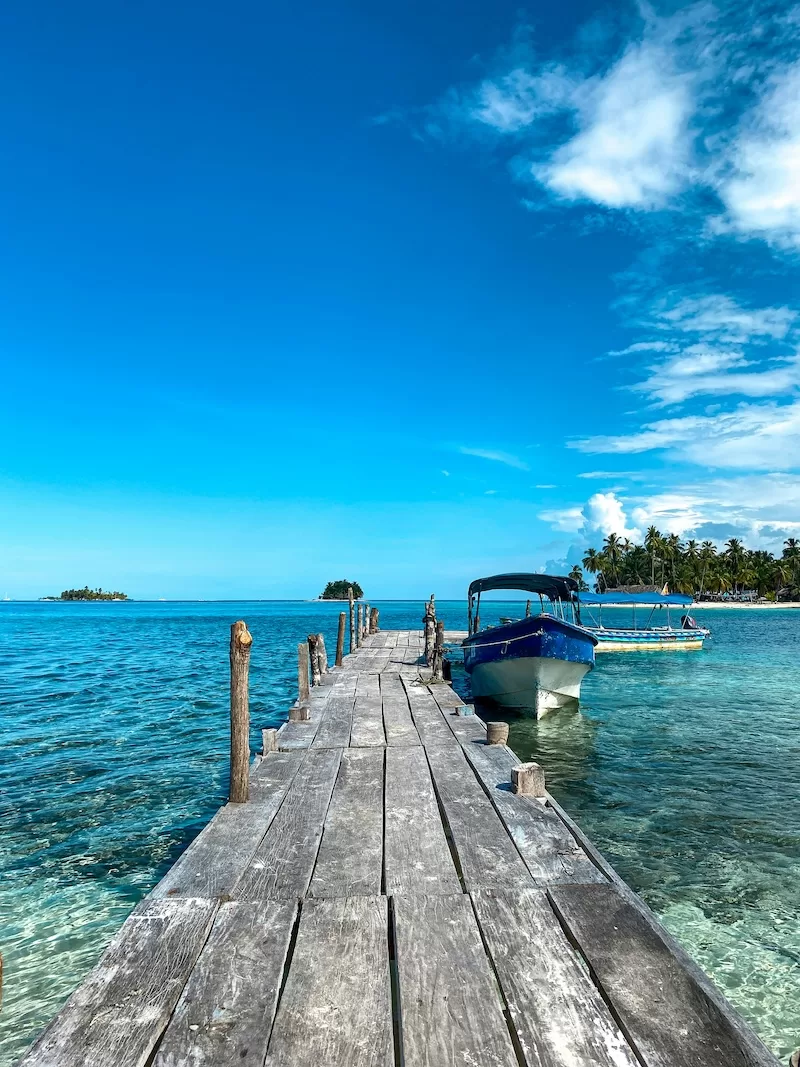 Wooden dock leading to a moored boat in the clear turquoise waters of the San Blas Islands, Panama