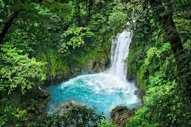 Waterfall cascading into a turquoise pool surrounded by dense rainforest in Costa Rica