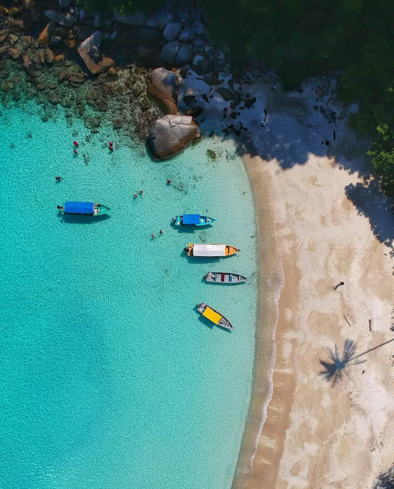 Aerial view of a turquoise cove with colorful boats anchored near a white sand beach
