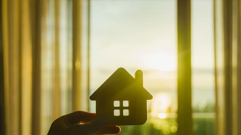 House-shaped cutout held against a bright window at sunset