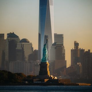 The Statue of Liberty at sunset with the Freedom Tower and Lower Manhattan skyline in the background