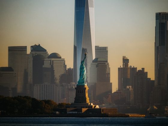 The Statue of Liberty at sunset with the Freedom Tower and Lower Manhattan skyline in the background