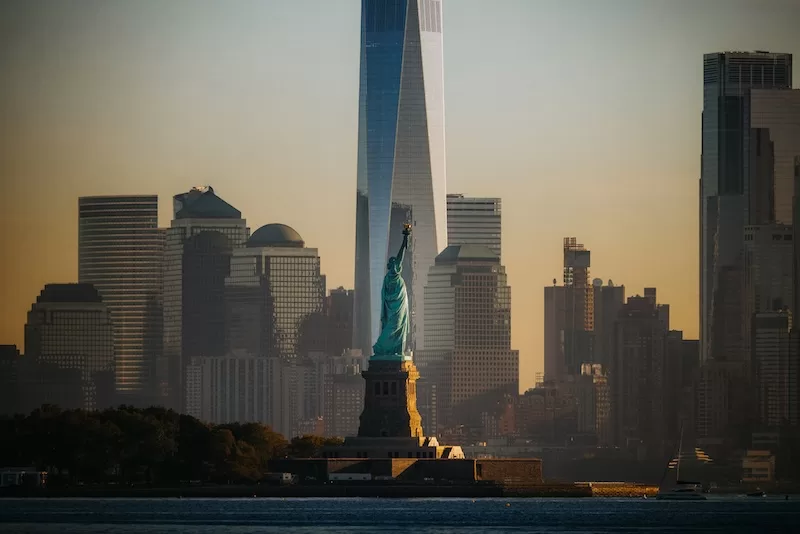 The Statue of Liberty at sunset with the Freedom Tower and Lower Manhattan skyline in the background