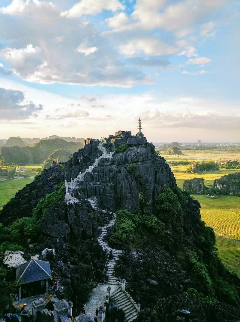 Stone staircase winding up a rocky mountain peak in Ninh Binh, Vietnam, with a pagoda at the summit