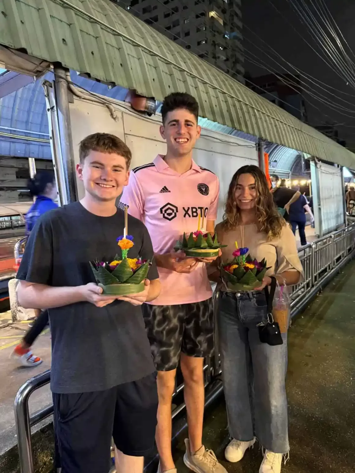 Three young expats holding traditional floral arrangements during a celebration in Bangkok