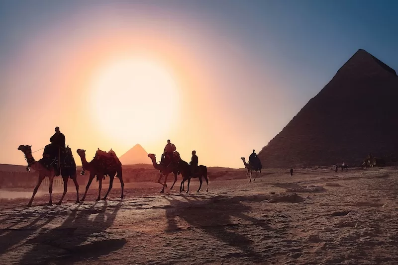Camel riders beside the Pyramids of Giza at sunset in Egypt