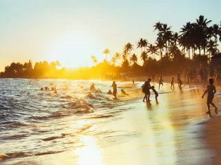 A crowded Brazilian beach at sunset, families playing in the surf under palm trees: where the story of moving from Brazil to Europe begins