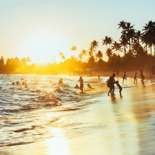 A crowded Brazilian beach at sunset, families playing in the surf under palm trees: where the story of moving from Brazil to Europe begins