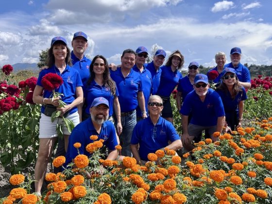 Chair the Love volunteers in blue polos gathered in a field of marigolds and celosia during a distribution trip