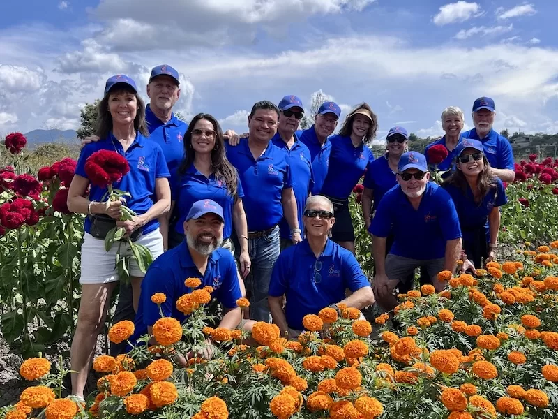 Chair the Love volunteers in blue polos gathered in a field of marigolds and celosia during a distribution trip