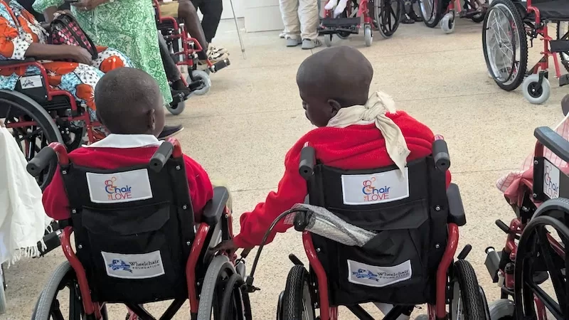 Two children in their new red wheelchairs hold hands during a distribution.