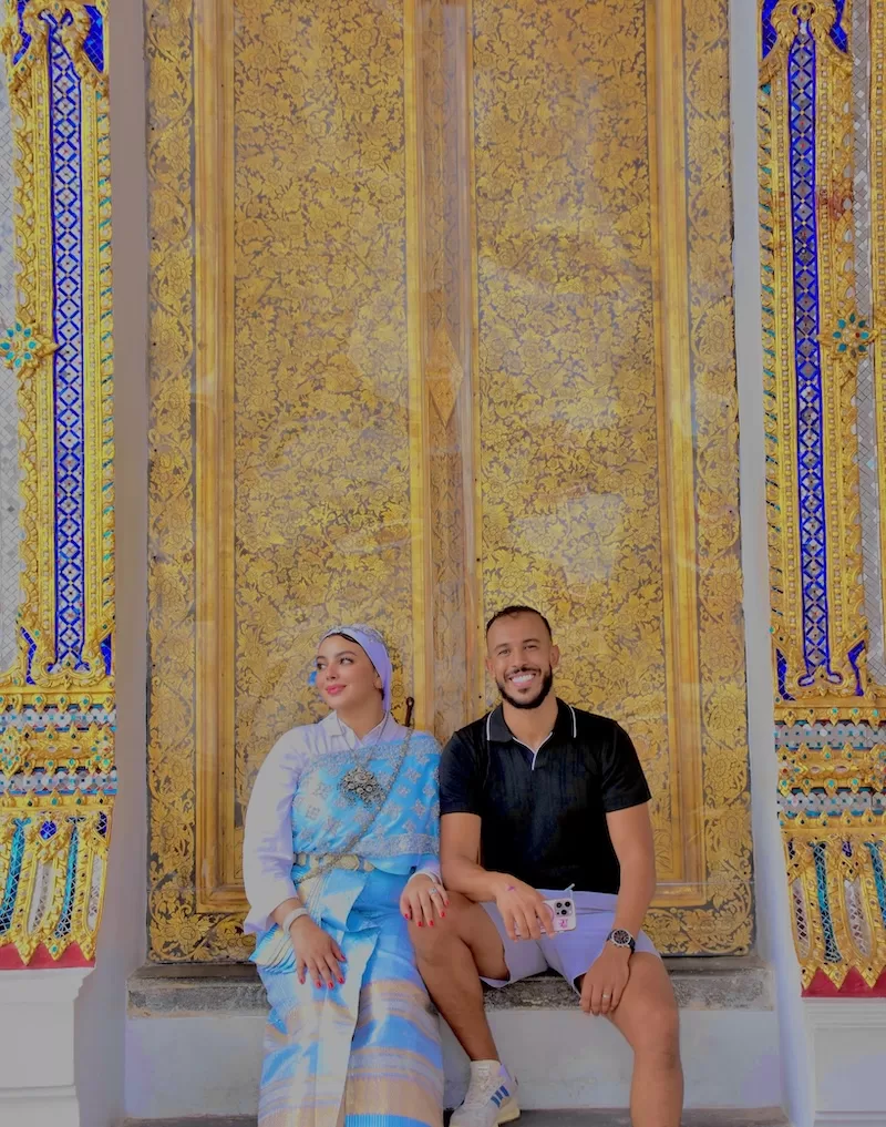 Anis and his wife sit before a gilded temple door in Bangkok.