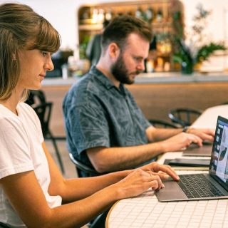 Two remote workers on laptops in a cafe, illustrating digital nomad visa options in 2026