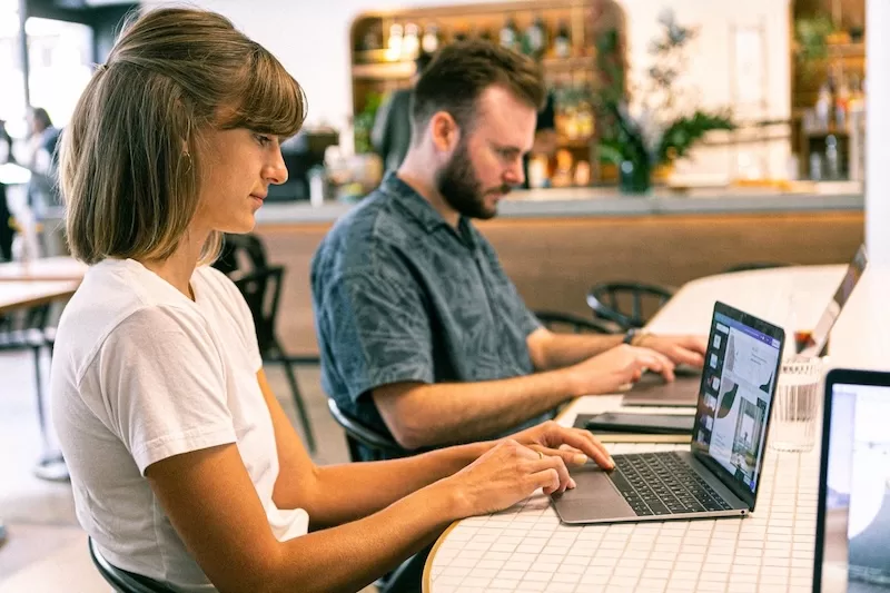 Two remote workers on laptops in a cafe, illustrating digital nomad visa options in 2026