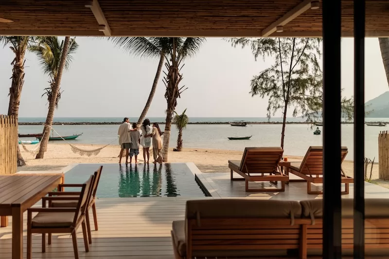 A family stands at the pool edge of a beachfront home, looking out to sea.