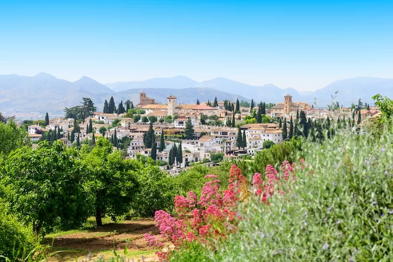The white houses and towers of Granada’s Albaicín spill down a green hillside.