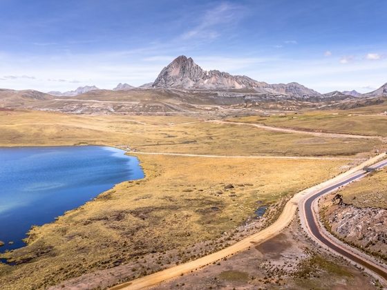 Winding road beside a blue lake with a mountain peak