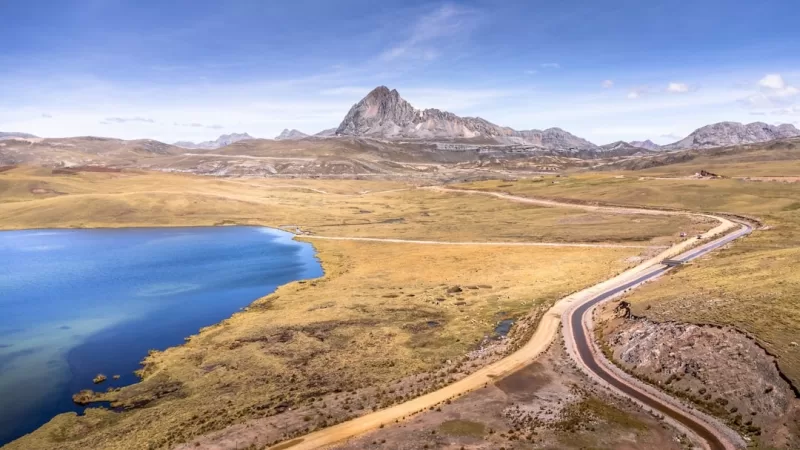 Winding road beside a blue lake with a mountain peak